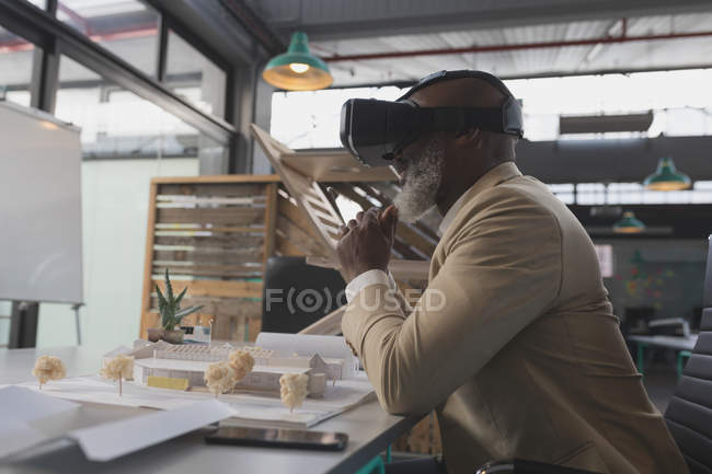 Male executive using virtual reality headset at table in office — Stock Photo