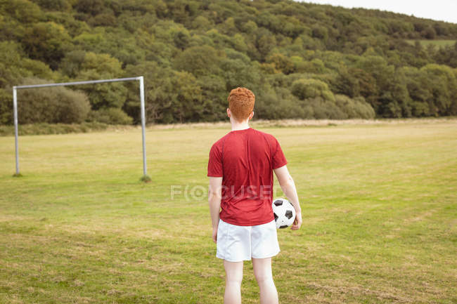 Вид сзади футболиста, стоящего с футбольным мячом на поле — стоковое фото
