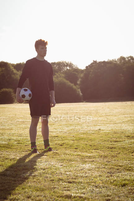Футболист стоит с футбольным мячом в поле в солнечный день — стоковое фото