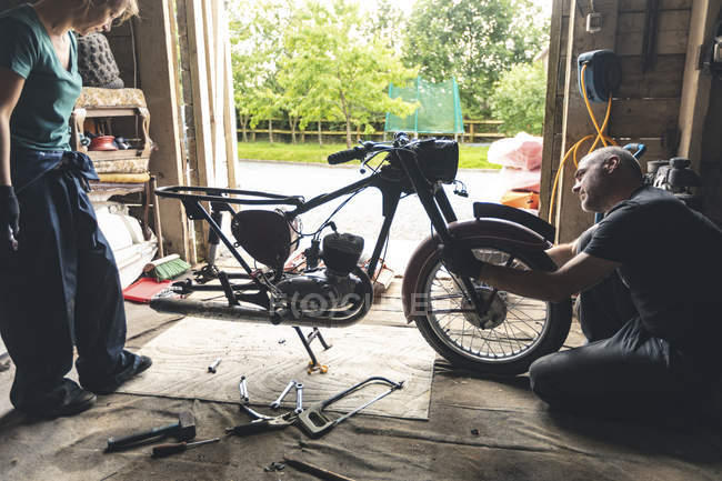 Meccanici di sesso maschile e femminile che riparano moto in officina — Foto stock