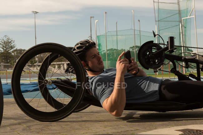 Вид сбоку спортсмена-инвалида с помощью мобильного телефона в инвалидной коляске — стоковое фото