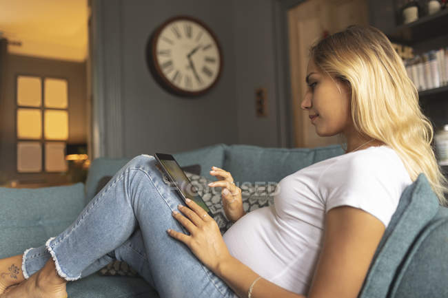 Gros plan de la femme enceinte utilisant une tablette numérique sur le canapé — Photo de stock
