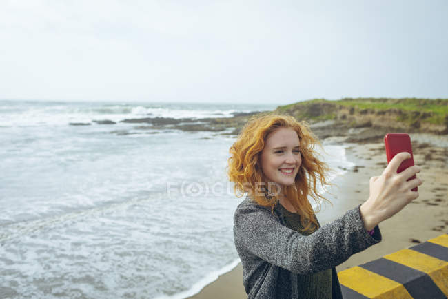 Donna rossa che si fa selfie con il cellulare in spiaggia
. — Foto stock