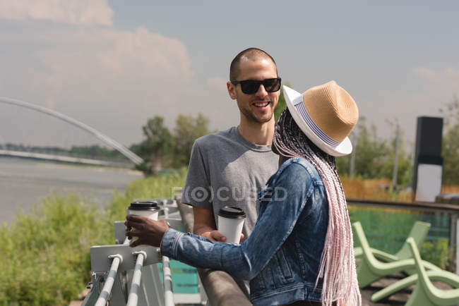 Couple with coffee cups standing near railings outdoors — Stock Photo