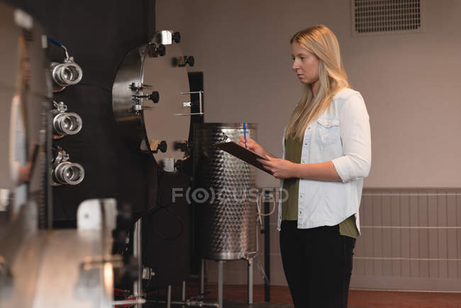 Beautiful female worker examining distillery tank in factory — Stock Photo