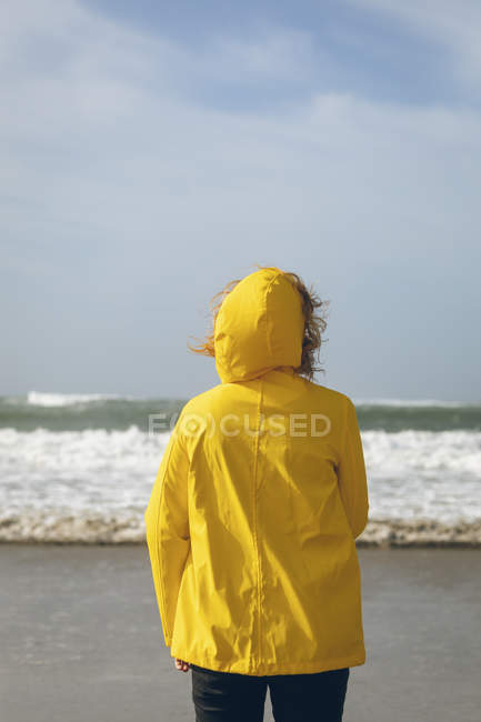 Vue arrière de la femme en veste jaune debout sur la plage . — Photo de stock