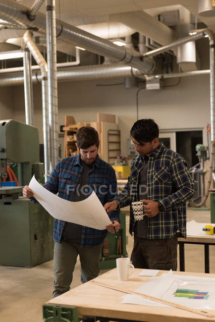 Zwei Handwerker diskutieren in Werkstatt über Bauplan — Stockfoto