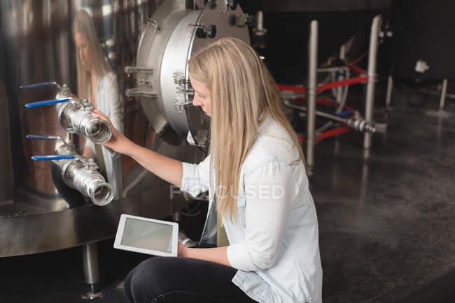Young female worker examining distillery tank in factory — Stock Photo