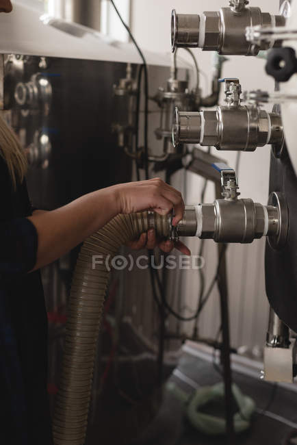 Mid section of female worker checking pipe of distillery tank — Stock Photo