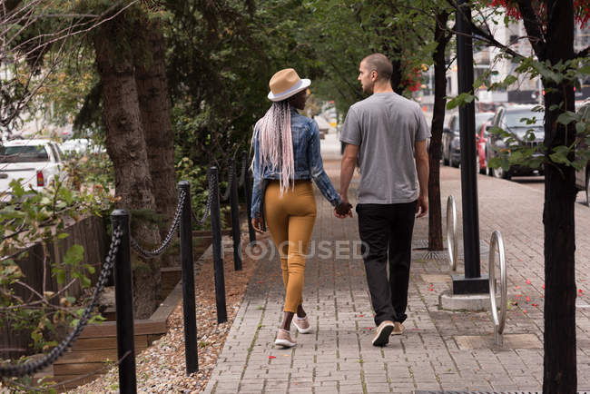 Vista trasera de pareja caminando por la acera en la ciudad - foto de stock
