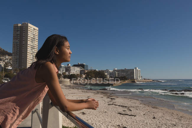 Vista laterale della donna appoggiata sulla ringhiera vicino alla spiaggia — Foto stock