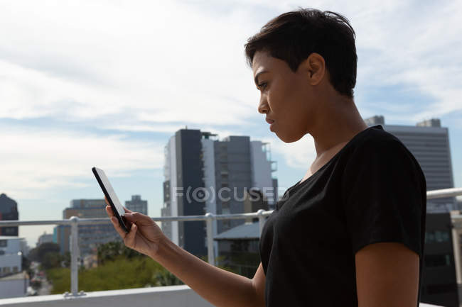 Vue latérale de la femme adulte moyenne utilisant le téléphone mobile sur la terrasse . — Photo de stock