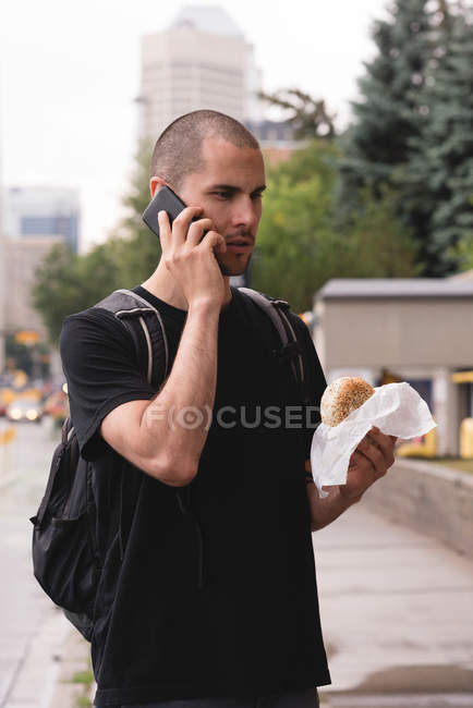Primer plano del joven con hamburguesa hablando por teléfono móvil - foto de stock
