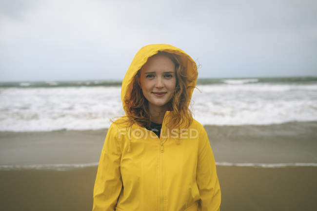 Ritratto di donna rossa in giacca gialla in piedi in spiaggia . — Foto stock