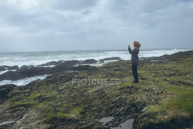 Вид збоку руда жінка фотографує з мобільним телефоном на пляжі . — стокове фото