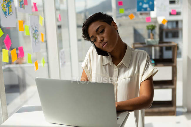 Executivo de negócios falando no telefone celular enquanto usa laptop no escritório . — Fotografia de Stock