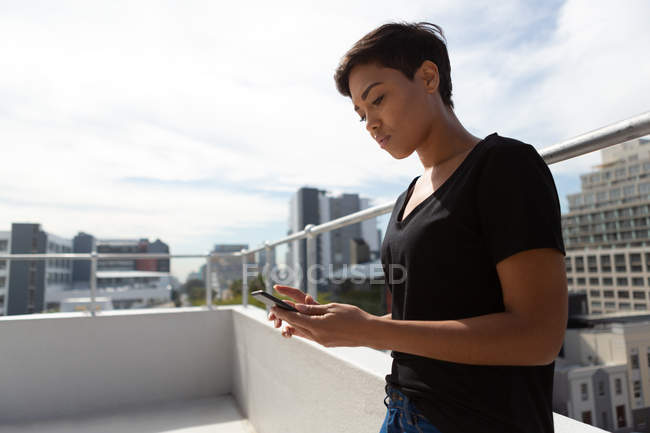 Vista lateral de la mujer adulta media usando teléfono móvil en la terraza . - foto de stock
