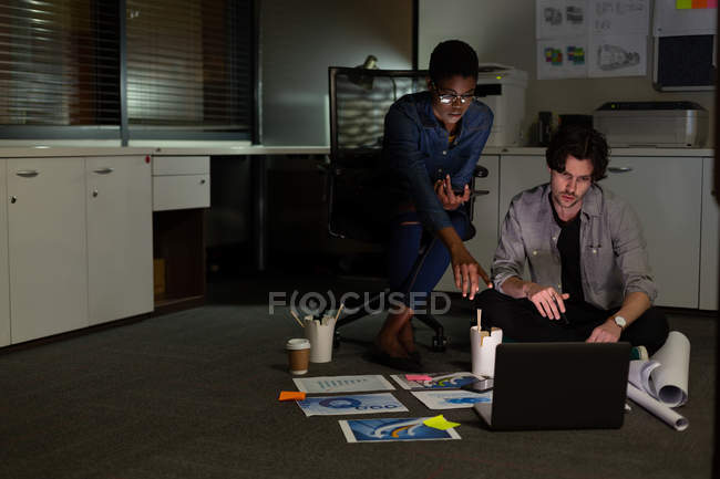 Ejecutivos discutiendo sobre el ordenador portátil en la oficina por la noche - foto de stock