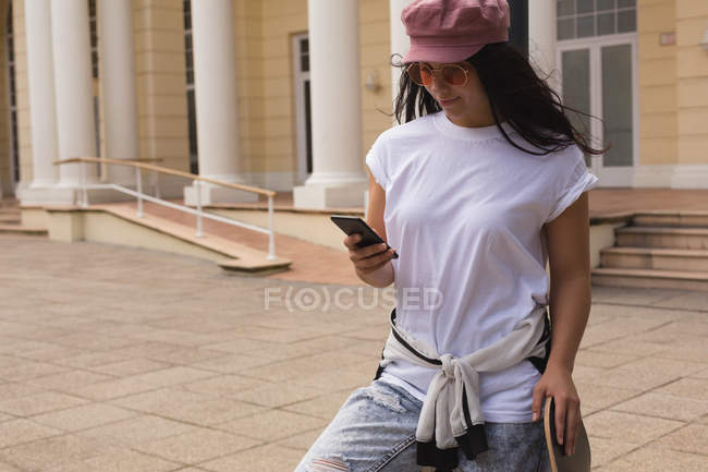 Schöne Skateboarderin benutzt Handy in der Stadt — Stockfoto