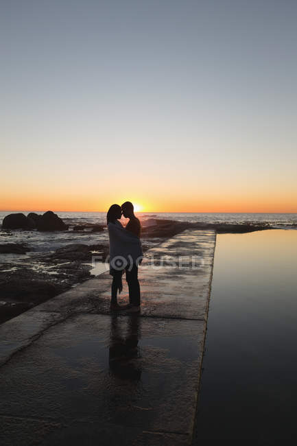 Пара обіймає один одного на набережній під час заходу сонця — стокове фото