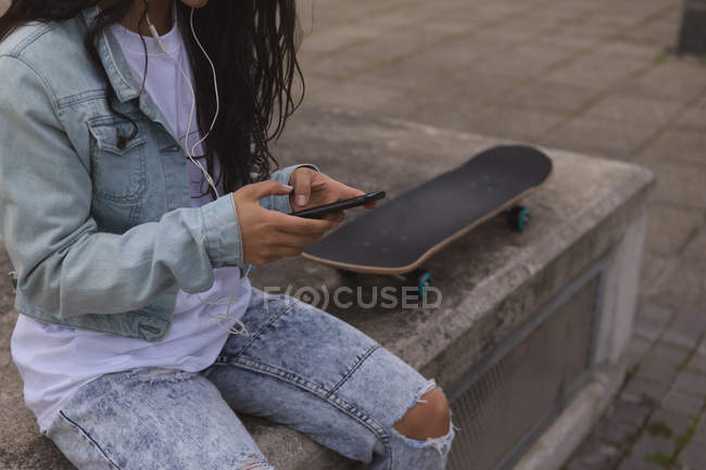 Середина жіночого скейтбордера, що використовує мобільний телефон у місті — стокове фото