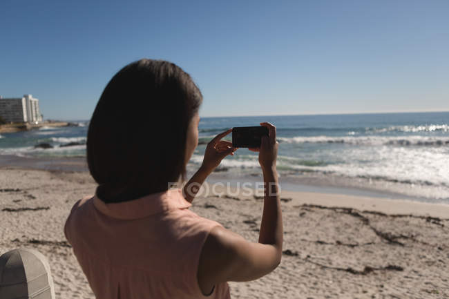 Вид сзади женщины, фотографирующей с мобильного телефона рядом с пляжем — стоковое фото