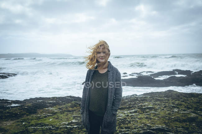 Руда жінка стоїть з руками в кишенях на пляжі . — стокове фото
