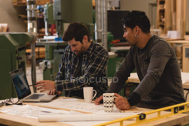 Dos artesanos atentos discutiendo sobre el portátil en el taller - foto de stock