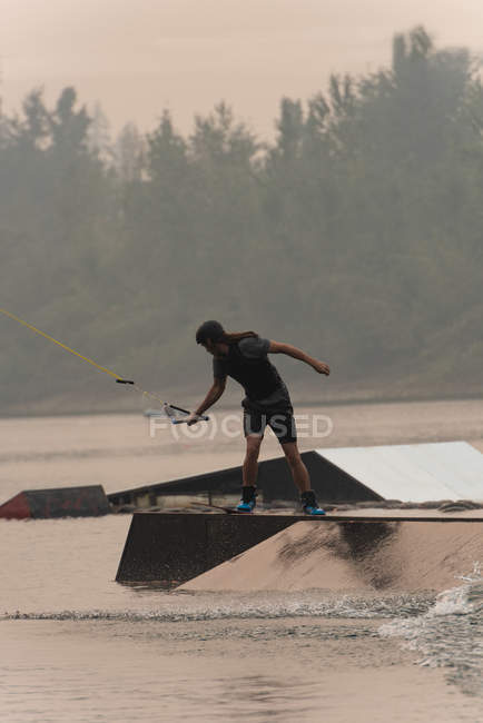 Jovem atleta wakeboarding no rio ao entardecer — Fotografia de Stock