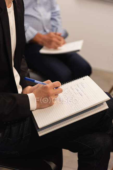 Mid section of executives writing on notepad in office — Stock Photo