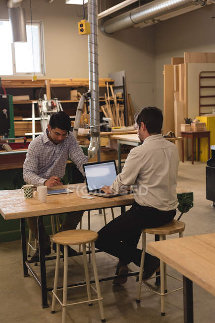 Deux artisans utilisant une tablette numérique et un ordinateur portable en atelier — Photo de stock