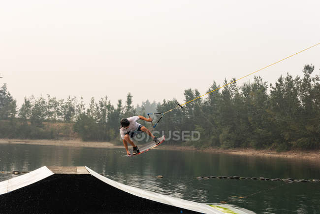 Homem adulto médio wakeboarding da rampa na água do rio — Fotografia de Stock