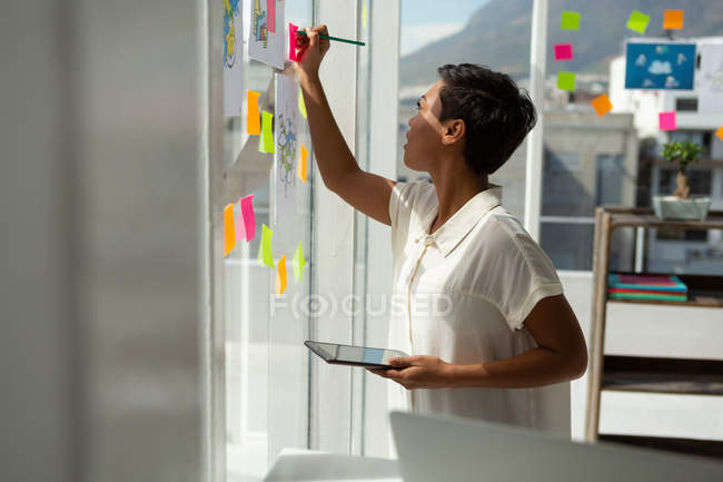 Vista lateral do executivo de negócios escrevendo em nota pegajosa no escritório . — Fotografia de Stock