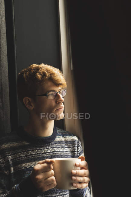 Homme prenant un café tout en regardant par la fenêtre à la maison — Photo de stock