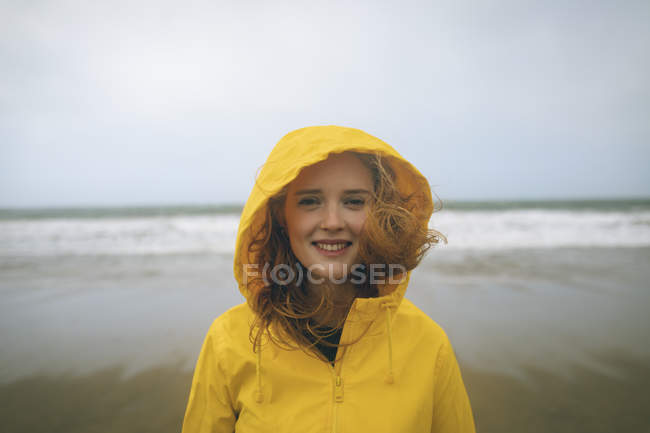 Retrato de mulher ruiva em casaco amarelo em pé na praia . — Fotografia de Stock