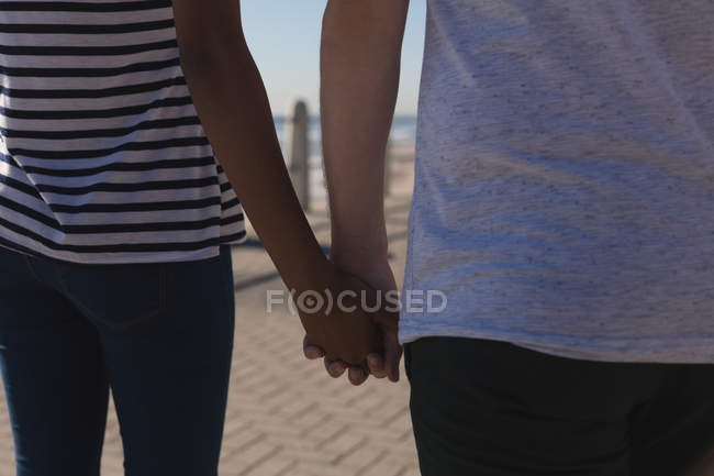 Средняя часть пары, держащихся за руки во время прогулки по набережной — стоковое фото