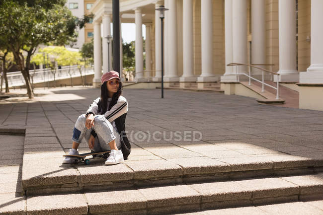 Female skateboarder sitting on skateboard in city — Stock Photo