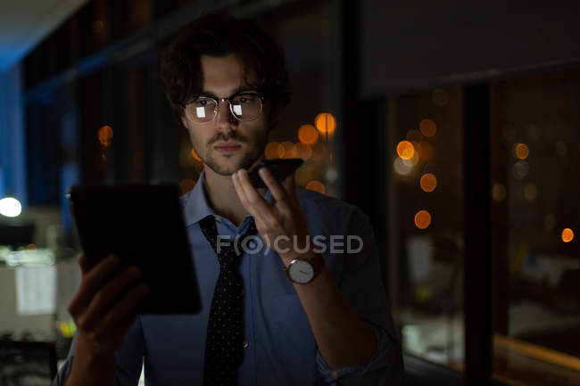 Male executive talking on mobile phone while using digital tablet in office at night — Stock Photo