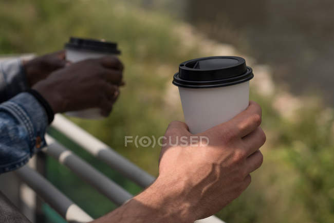 Close-up of couple with disposable cups leaning on railings — Stock Photo