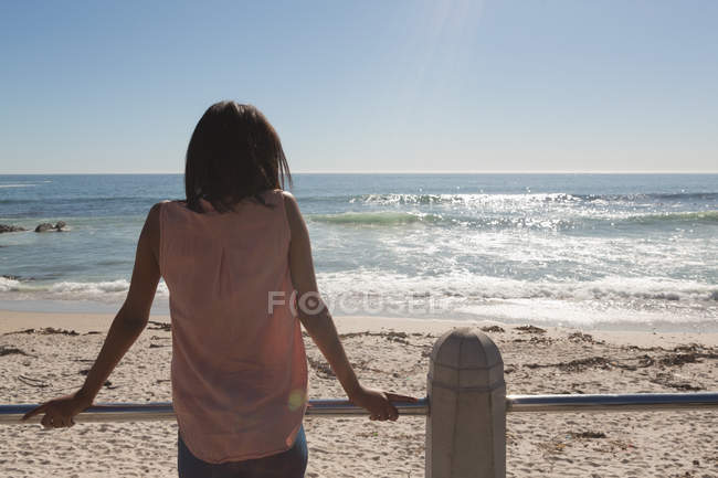 Вид ззаду жінки, що стоїть на набережній біля пляжу — стокове фото