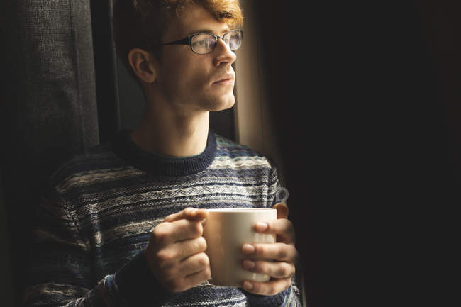 Man having coffee while looking through window at home — Stock Photo