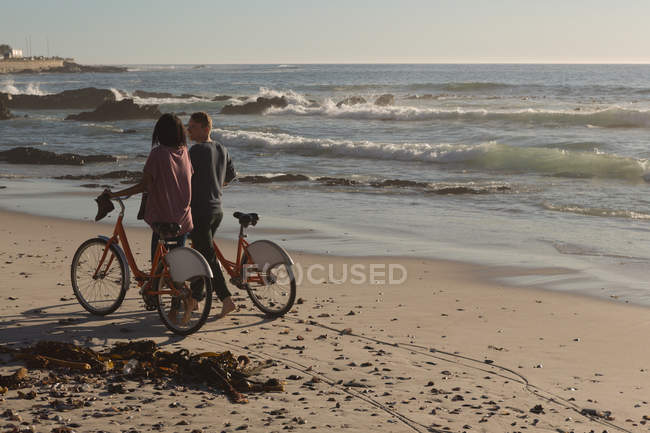 Casal com bicicletas andando na praia em luz suave — Fotografia de Stock
