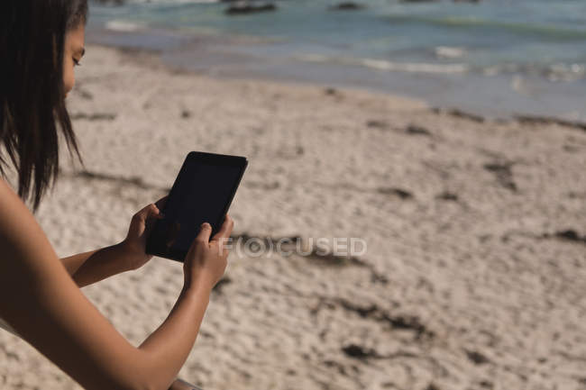Mujer usando tableta digital en la orilla del mar de arena - foto de stock