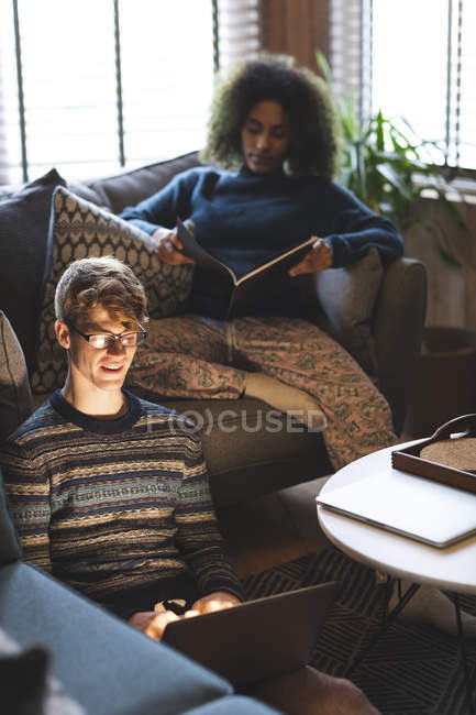 Couple utilisant ordinateur portable et livre de lecture dans le salon à la maison — Photo de stock