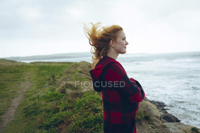 Продумана руда жінка стоїть з обіймами, схрещеними на пляжі . — стокове фото