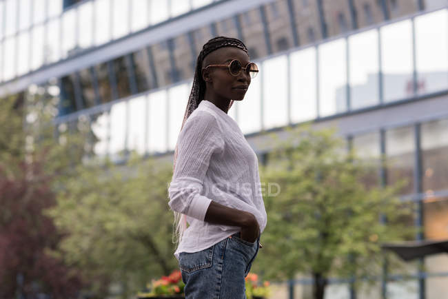 Jeune femme à la mode en lunettes de soleil debout en ville — Photo de stock