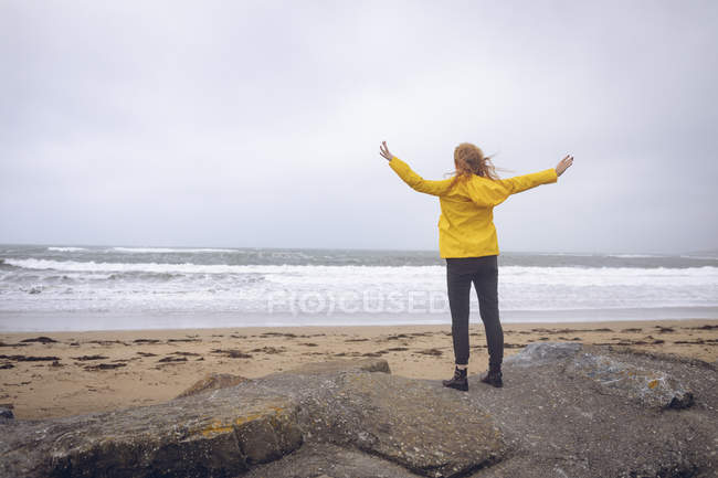 Вид ззаду на руду жінку, що стоїть з руками, витягнутими на пляжі . — стокове фото