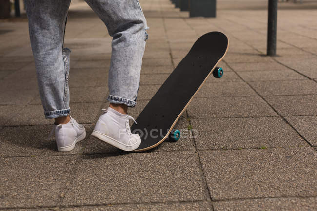 Low section of female skateboarder playing with skateboard in the city — Stock Photo