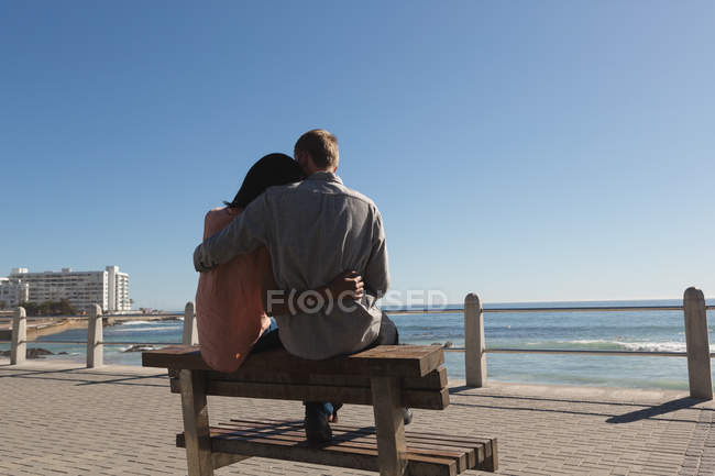 Vista trasera de la pareja sentada en el banco cerca de la playa - foto de stock