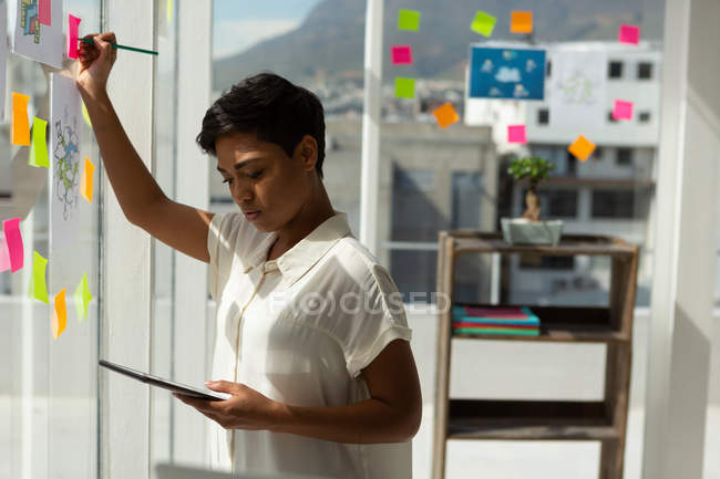 Бизнес-исполнительная запись на липкой ноте при использовании цифрового планшета в офисе . — стоковое фото